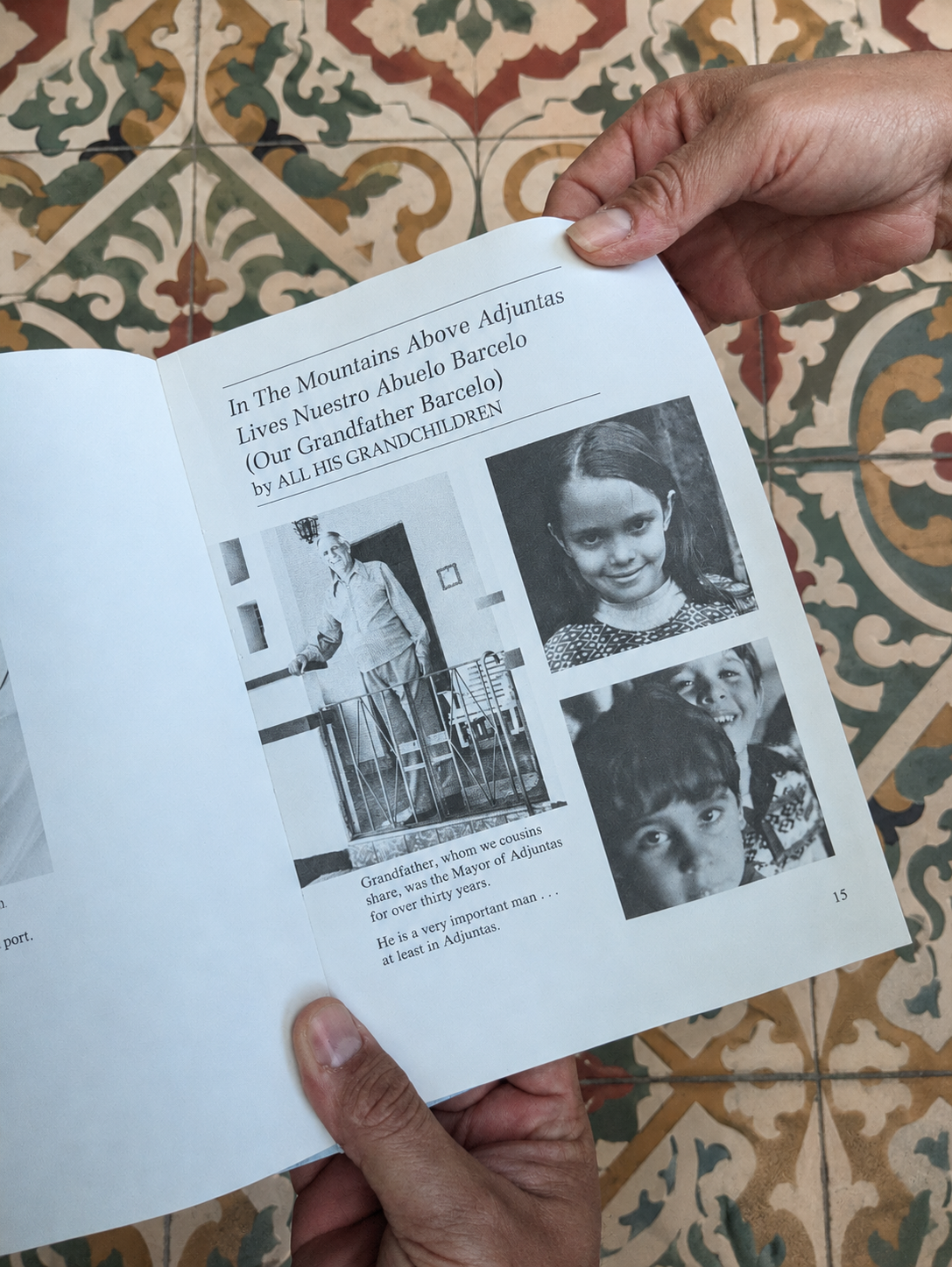 Hand holding a book open to a page with black and white photographs and text on a patterned tile background. Book about the story of the family that began growing coffee on the mountains of Adjuntas, Puerto RIco.