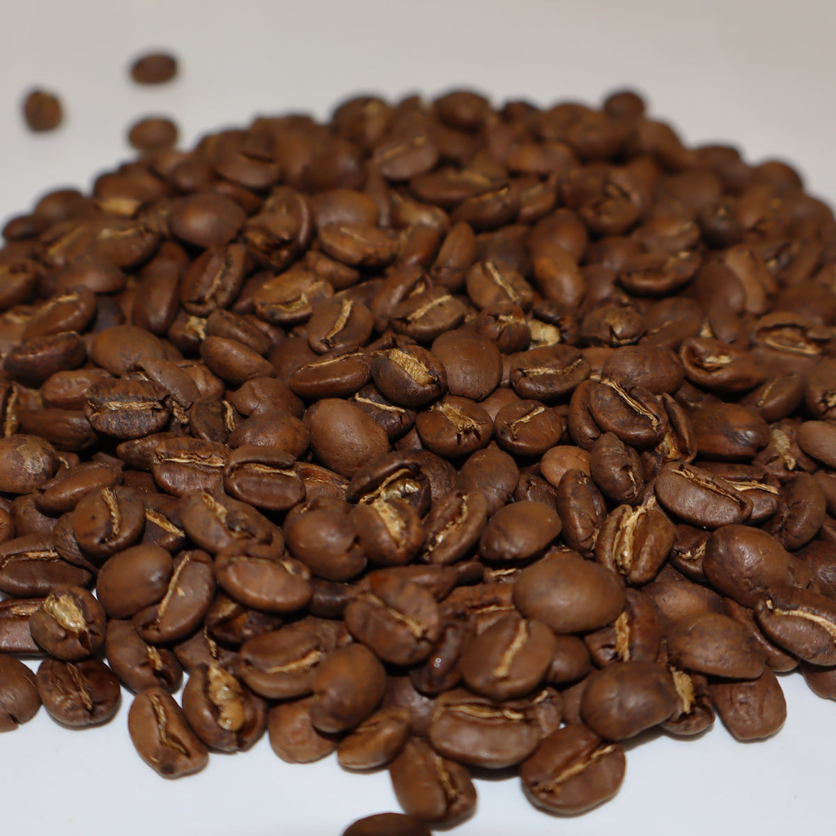 A pile of roasted coffee beans in medium to dark brown tones on a plain white background.